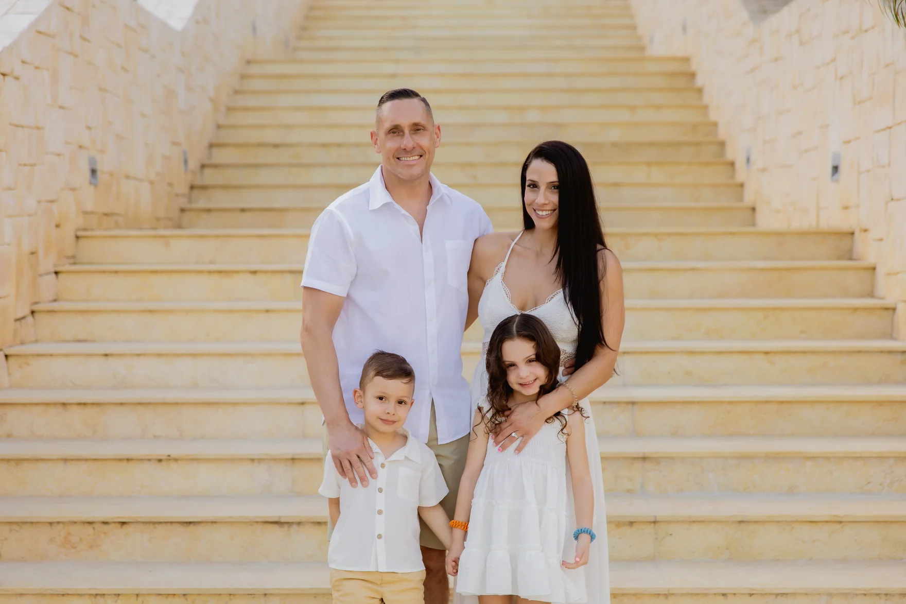Ryan and Jenny Fais with their two children on a grand stone staircase in warm light.